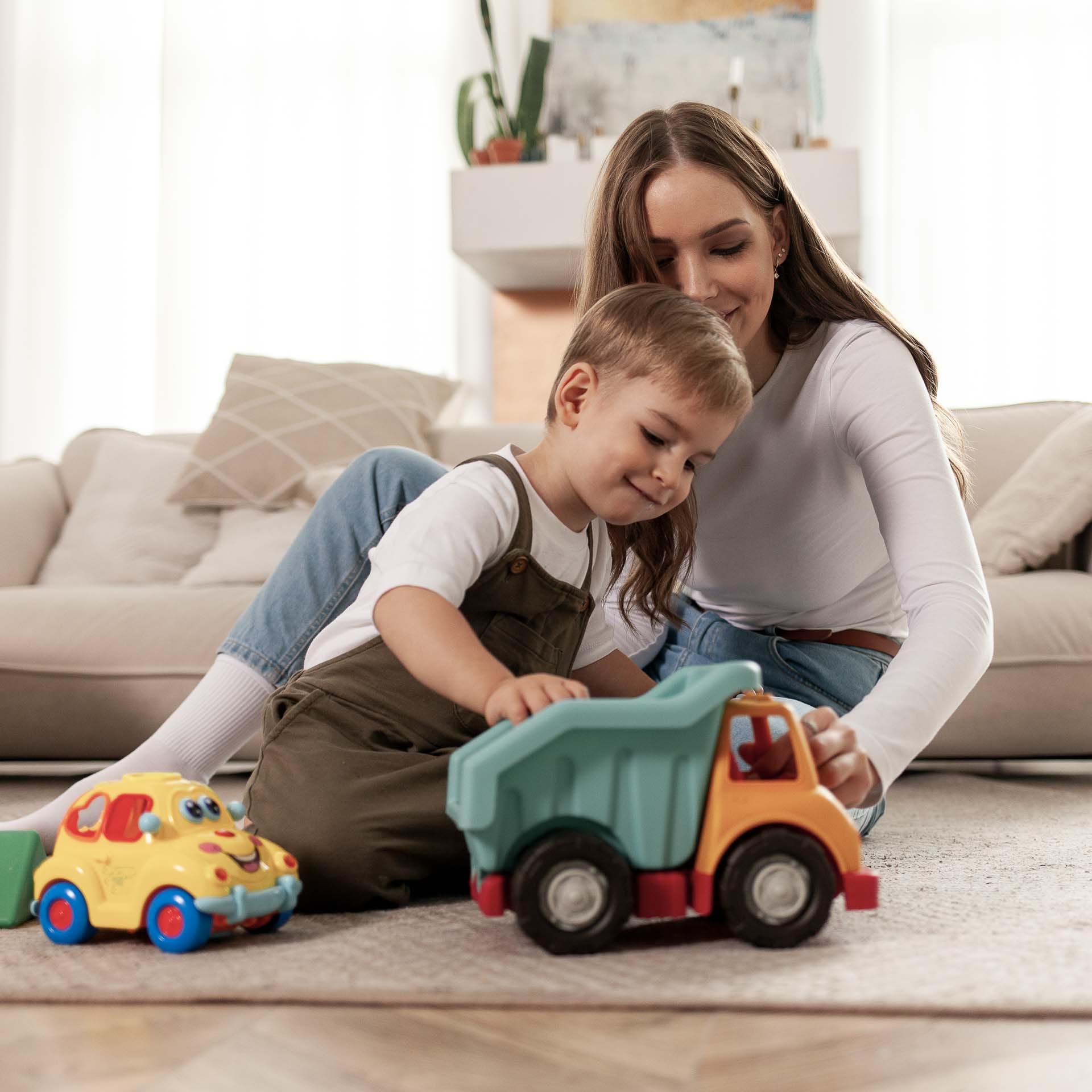 -Nuori nainen ja lapsi leikkivät autoilla lattialla.